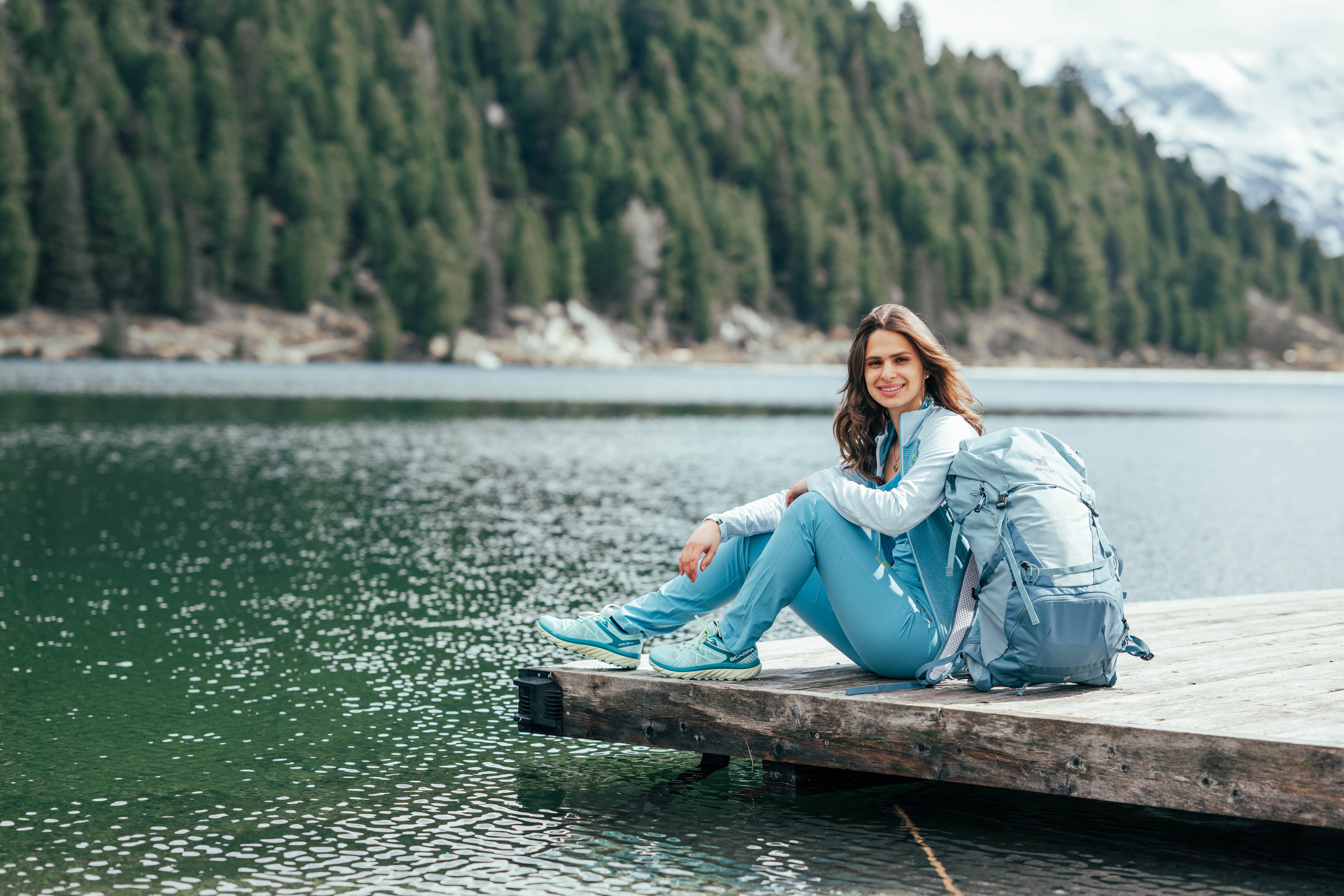Frau mit hellblauer Outdoorjacke auf einem Steg am Bergsee