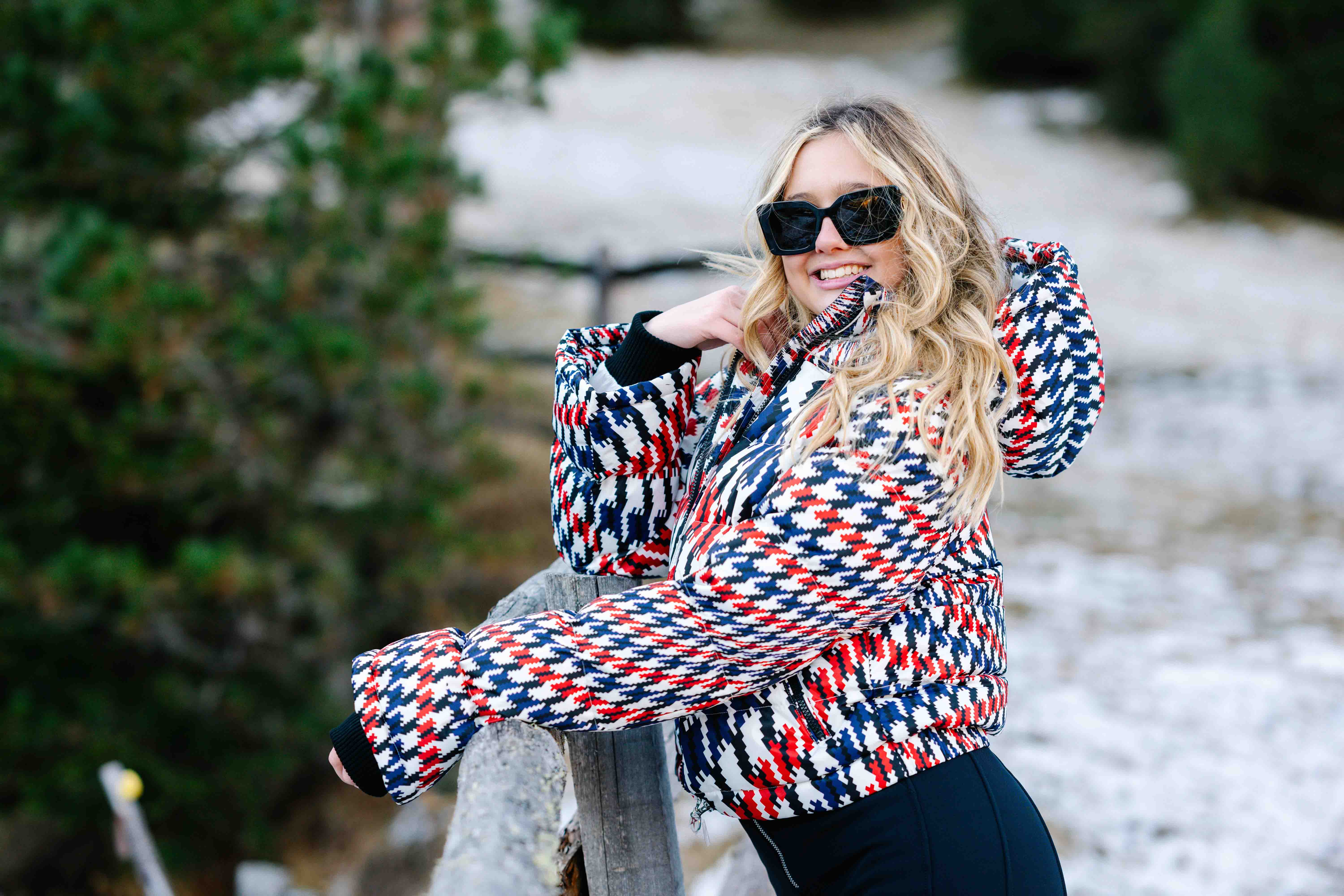 Frau mit bunt gemusterter Jacke und Sonnenbrille im Schnee