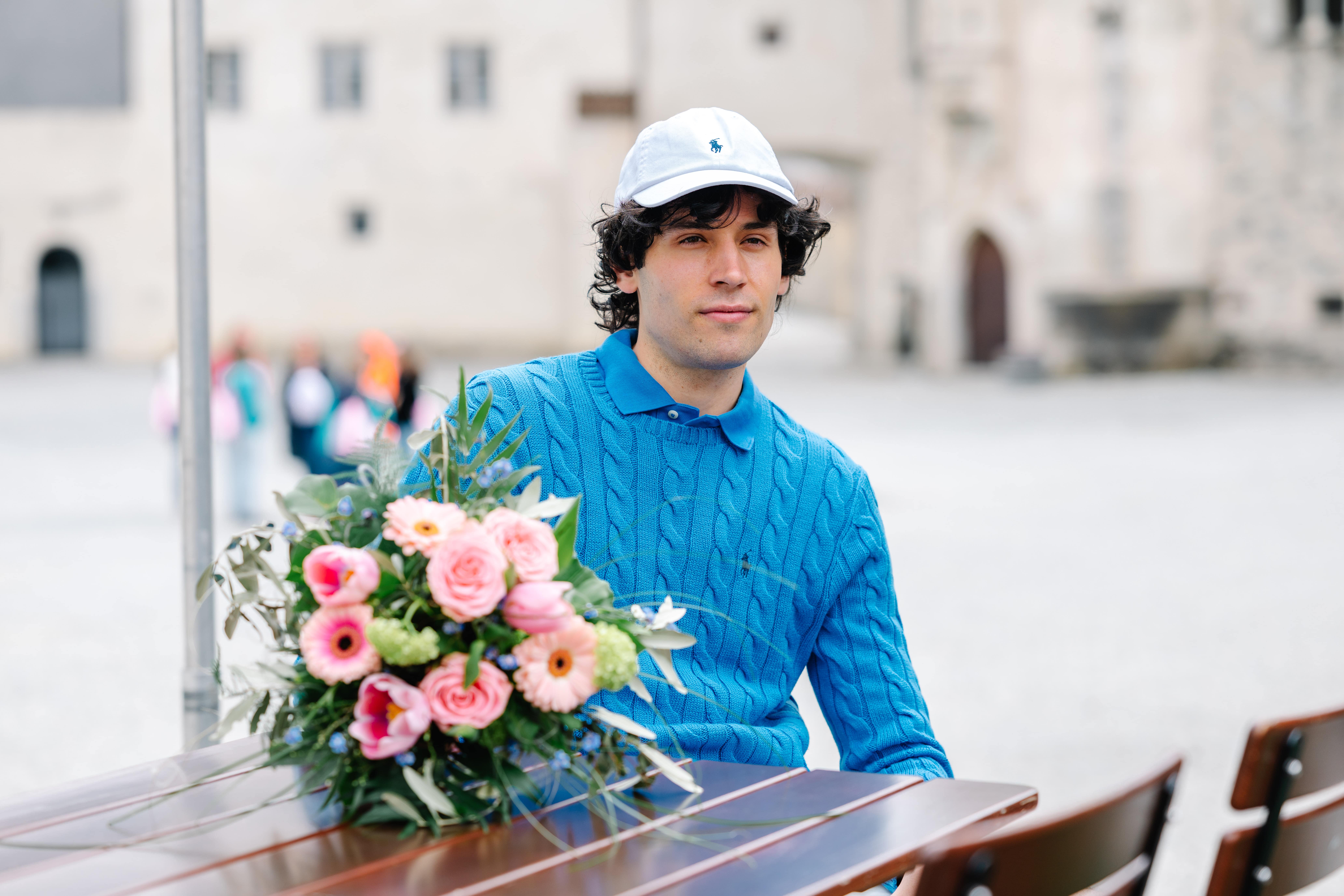 Mann mit blauem Pullover neben einem Blumenstrauß