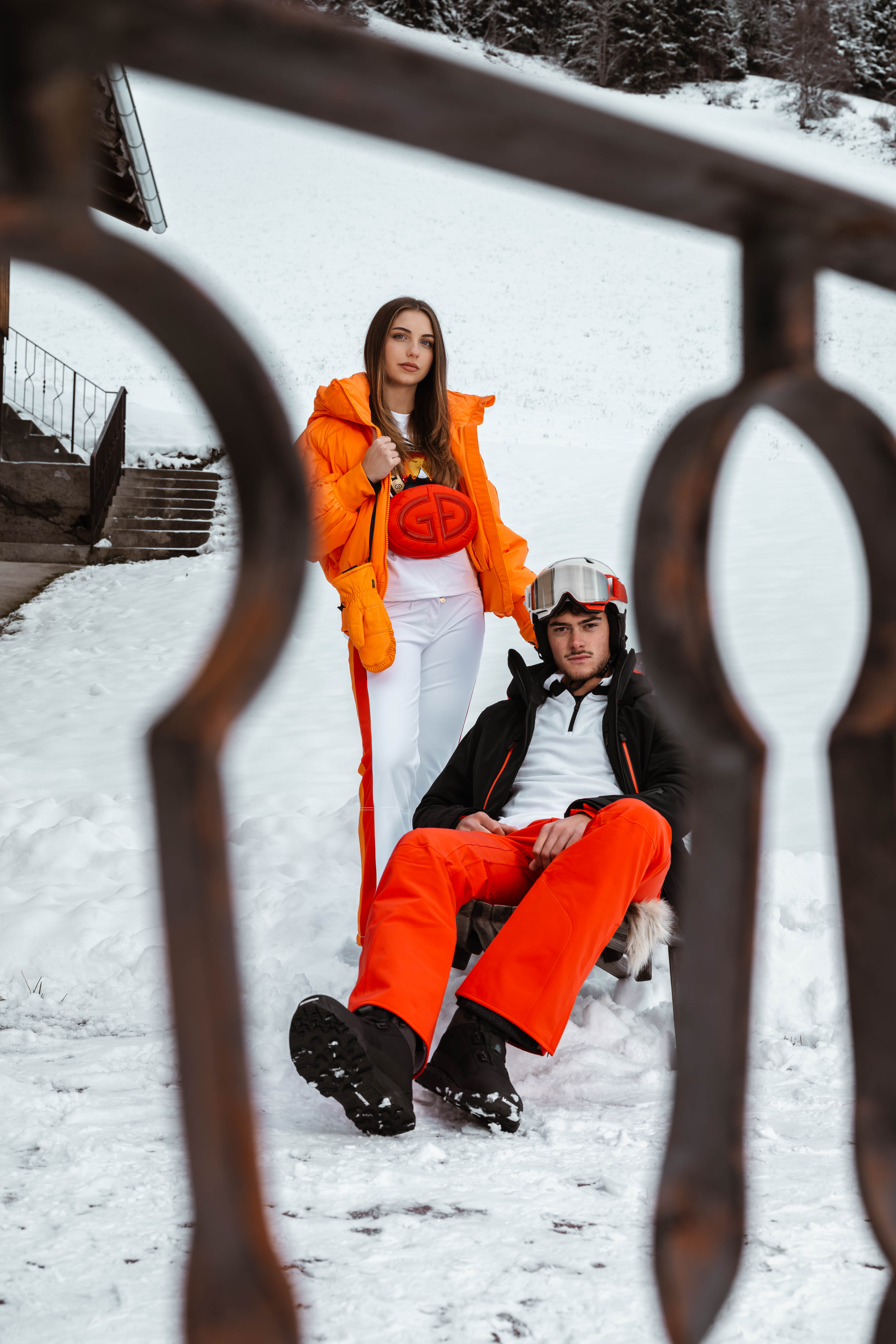 Zwei Personen in orange-roter Skibekleidung vor einer Hütte