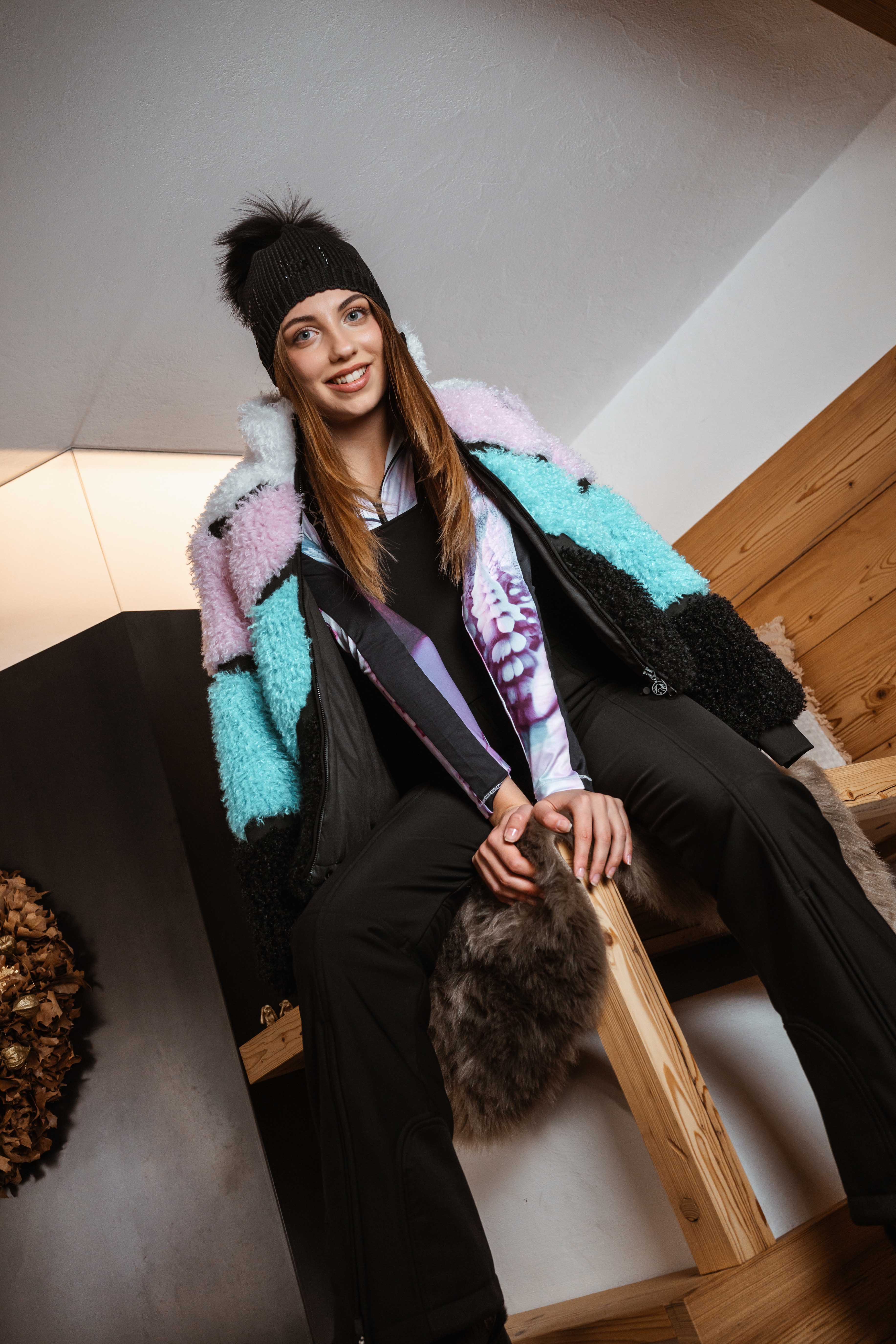 Frau mit mehrfarbiger Jacke, dunkler Mütze und Tasche